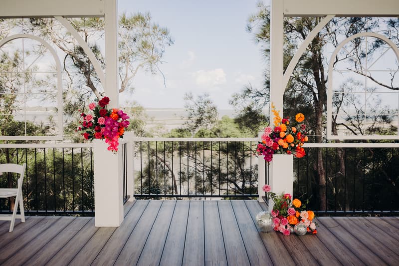 Empty pavilion area at Sandstone Point Hotel decorated with floral arrangements on white pillars overlooking trees and water in the background.