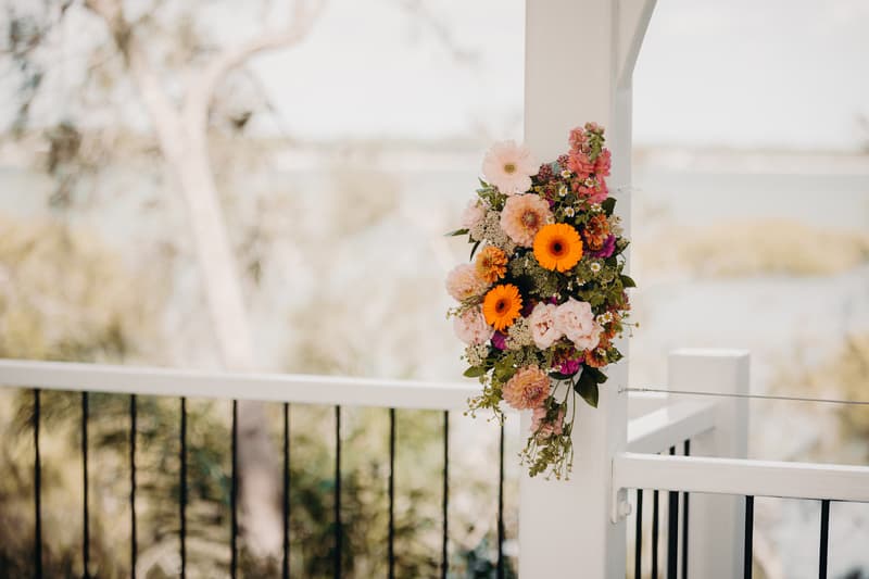 Floral arrangement with orange and pink flowers attached to a white pillar at Sandstone Point Hotel — Pavilion, overlooking a blurred natural outdoor background.
