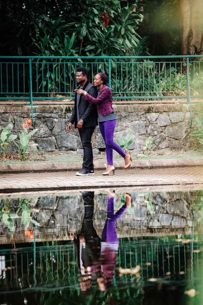 The couple walks along a path by a pond, reflected in the water, with lush greenery in Brisbane's City Botanic Gardens.