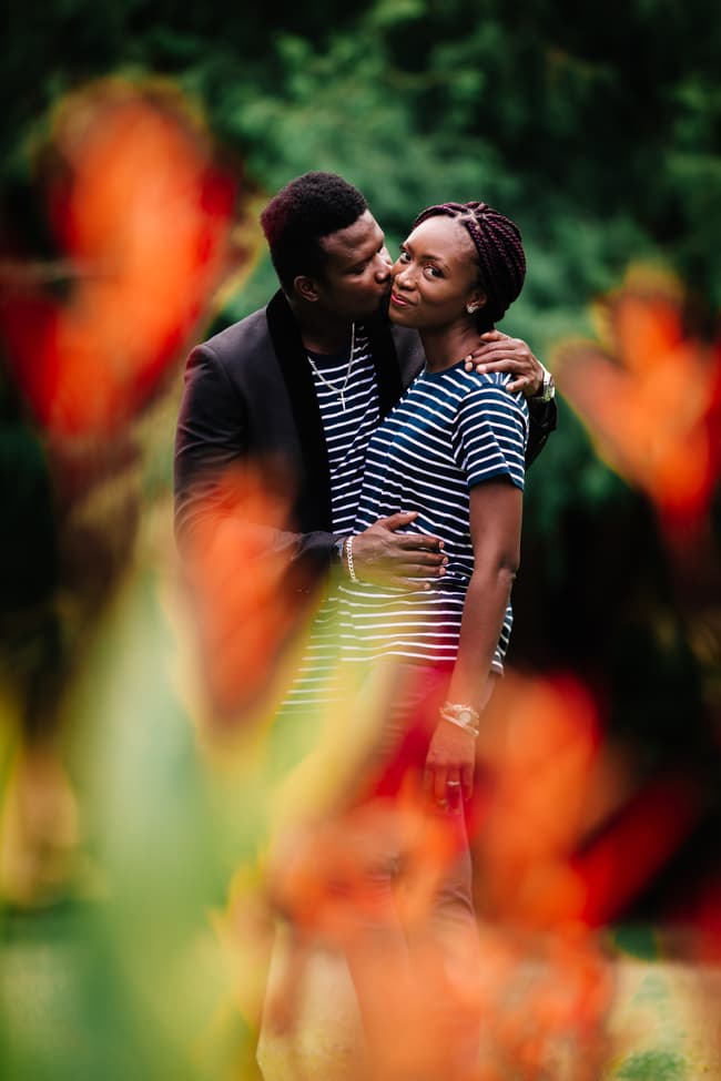 The couple shares a tender moment, with one whispering to the other, framed by vibrant flowers in Brisbane's City Botanic Gardens.