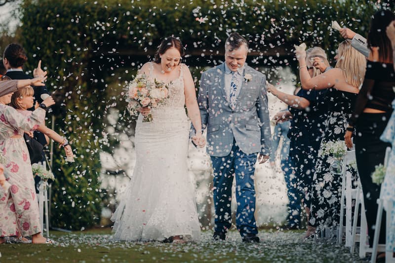 Bride Rebecca and groom Dale walk down the aisle at Sandstone Point Hotel — Rustic Arbour as guests throw flower petals.