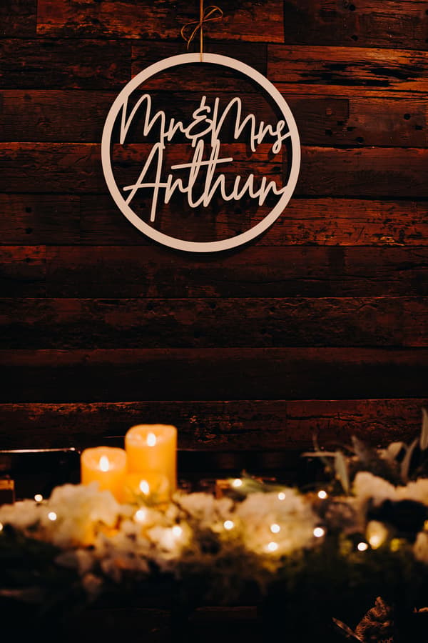 Decorative sign reading 'Mr & Mrs Anthony' hanging on a dark wooden wall above lit candles and floral arrangements at Ocean View Estates.