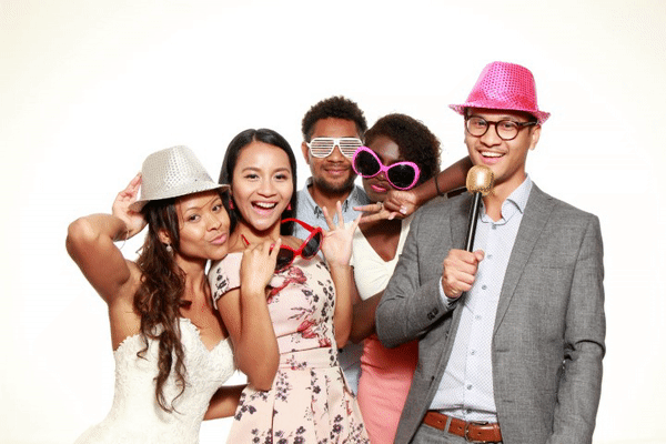 Group of guests wearing fun hats and sunglasses, posing playfully with a microphone.