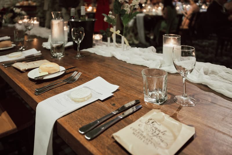 Reception table at Sandstone Point Hotel — The Cellar set with glassware, cutlery, bread rolls, candles, and wedding favors.