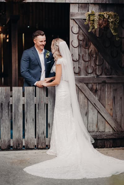 Krystal and Brandon hold hands and face each other near a rustic wooden gate decorated with horseshoes. Elopement photography Brisbane by She Said Yes.