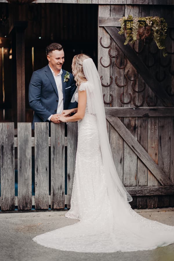Krystal and Brandon hold hands and face each other near a rustic wooden gate decorated with horseshoes at Sandstone Point Hotel.