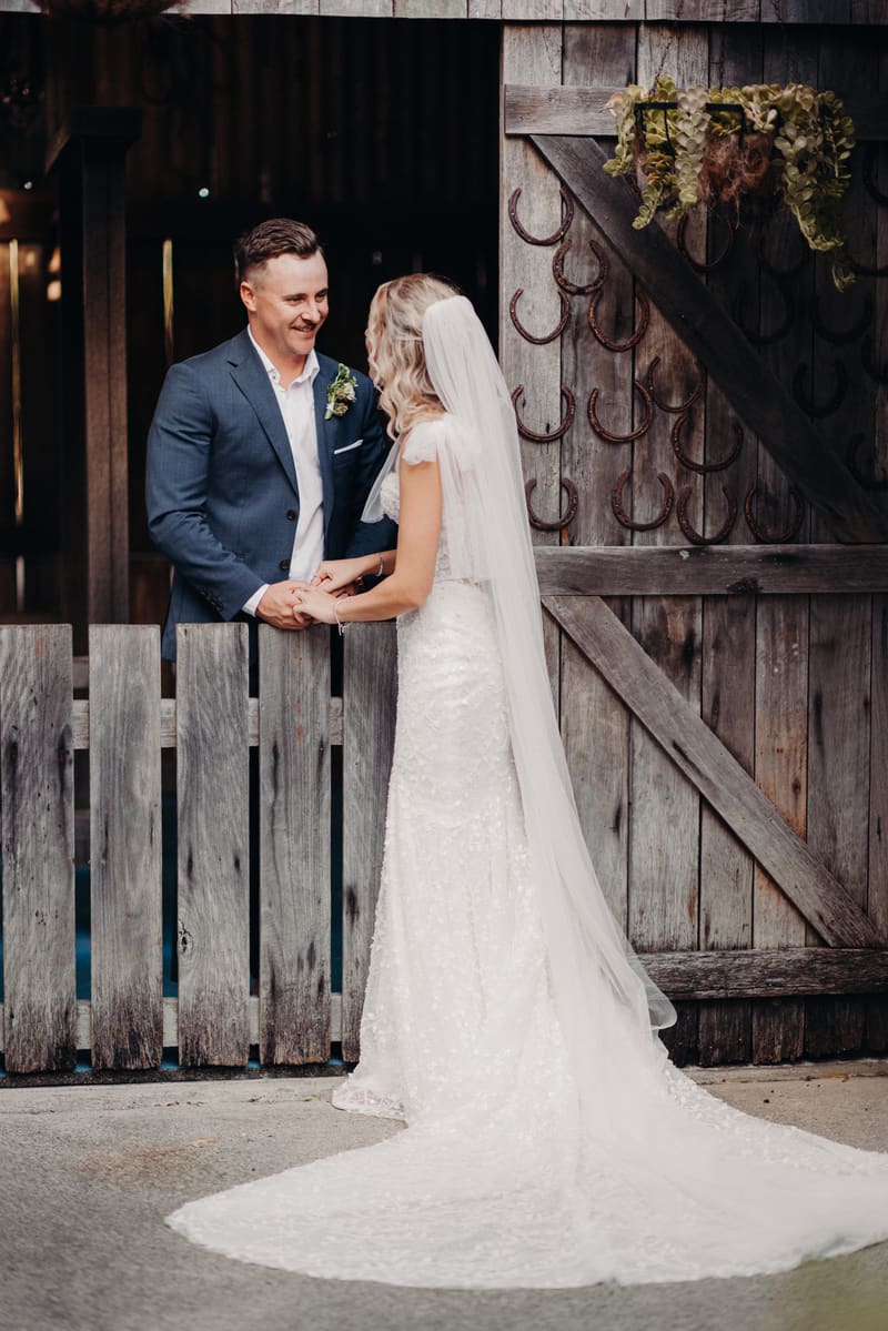 Krystal and Brandon hold hands and face each other near a rustic wooden gate decorated with horseshoes. Elopement photography Brisbane by She Said Yes.