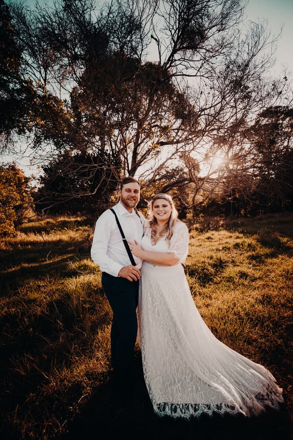 Annie and Trent pose together outdoors at Ocean View Estates during a styled couple portrait session with sunlight filtering through trees behind them.