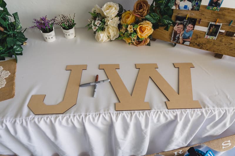 Wooden letters spelling 'J+W' on a white tablecloth at Bilinga Beach Weddings, accompanied by floral arrangements, small potted plants, and a photo display board.