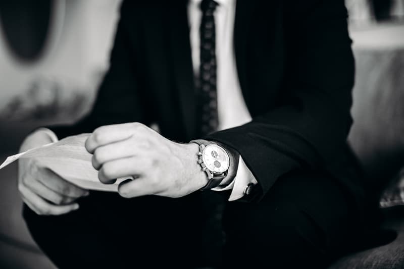 The groom Brent, dressed in a suit and tie, is seated and holding a piece of paper, with focus on his wristwatch at Preston Peak Winery Functions Centre.