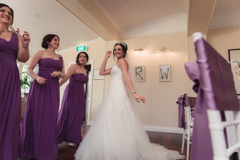 The bride Maryam poses smiling indoors at Hillstone St Lucia — The Quartyard with three bridesmaids in purple dresses standing nearby.