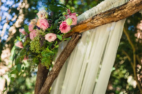 Close-up of a wooden wedding arch decorated with pink and white flowers and sheer white fabric at Kwila Lodge.