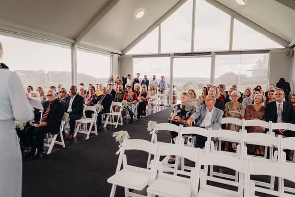 Guests seated in rows inside Preston Peak Winery Functions Centre, facing the ceremony area with a person speaking at the front left.