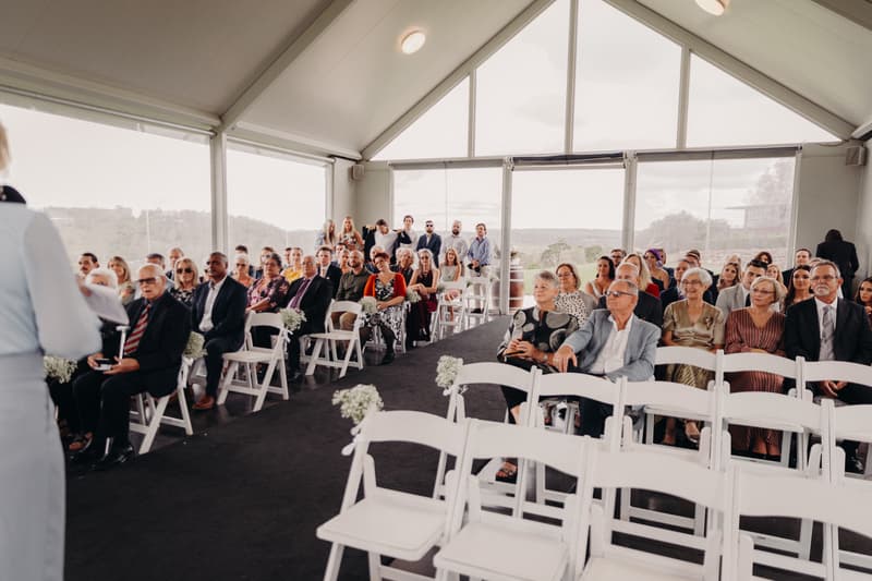 Guests seated in rows inside Preston Peak Winery Functions Centre, facing the ceremony area with a person speaking at the front left.