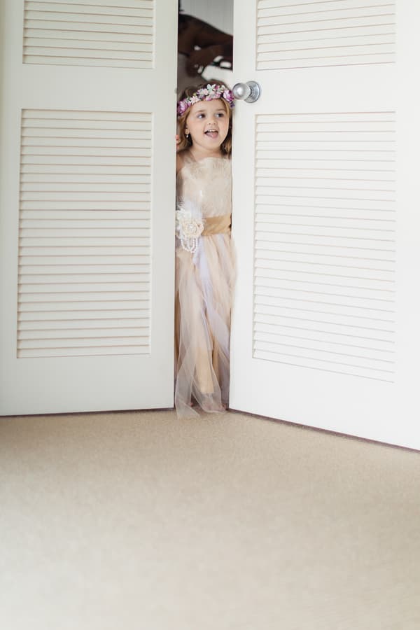 A flower girl peeks through partially open white louvered doors at Novotel Sunshine Coast Resort.