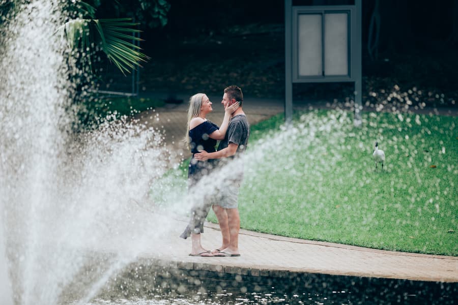 The couple embracing near a fountain, with water spray in the foreground at City Botanic Gardens.