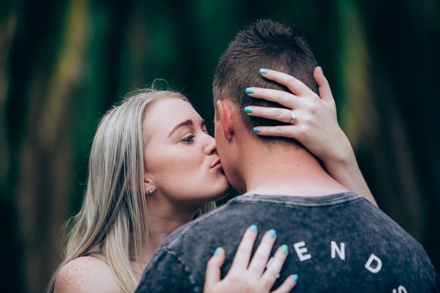 The couple sharing a kiss, with one wearing an engagement ring, at City Botanic Gardens.