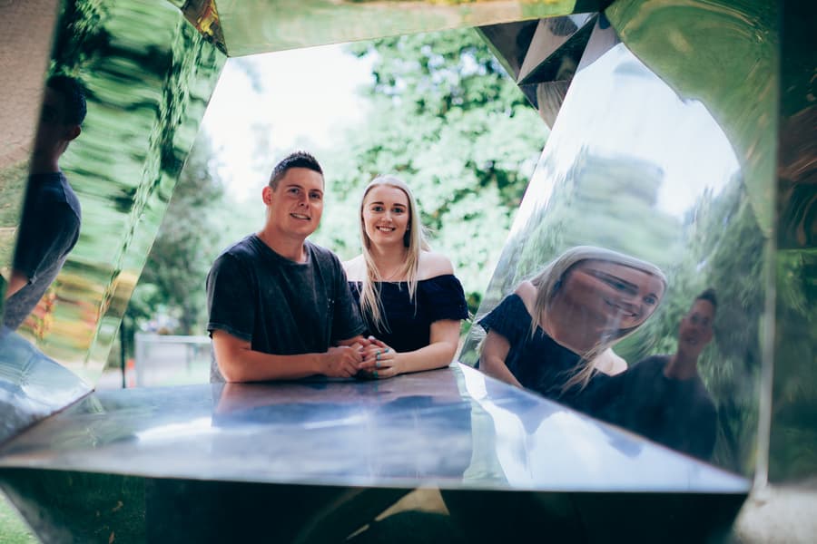 The couple sitting inside a reflective sculpture, smiling at the camera at City Botanic Gardens.
