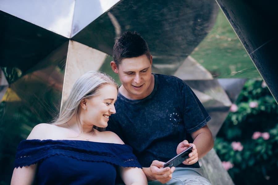 The couple looking at a phone together, sitting inside a reflective sculpture at City Botanic Gardens.