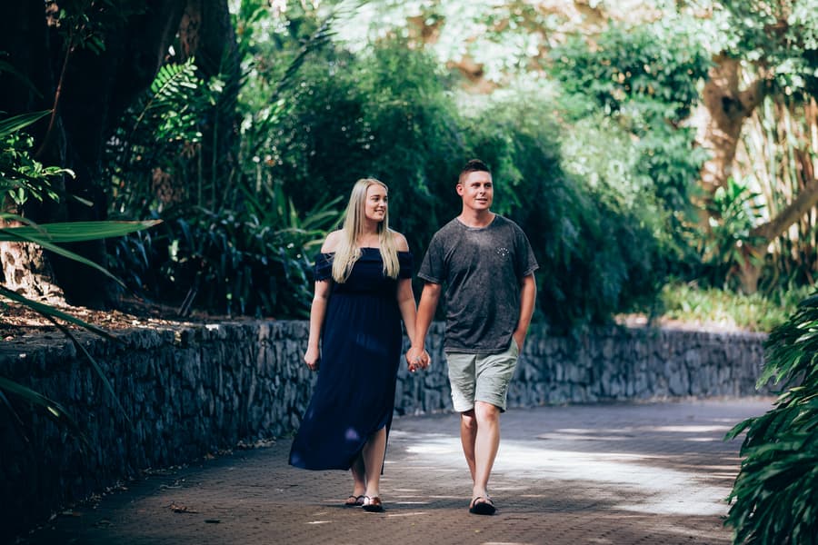 The couple walking hand in hand down a path, surrounded by greenery at City Botanic Gardens.
