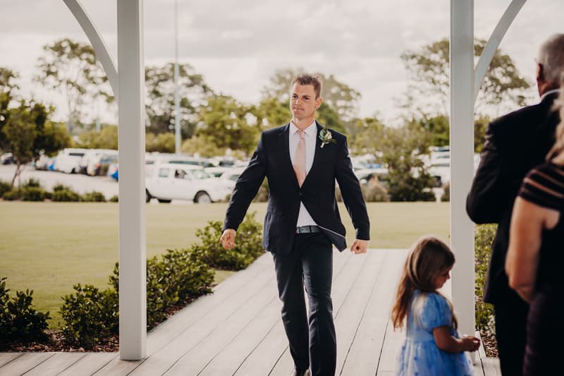 Ceremony pavilion at Sandstone Point Hotel with white chairs arranged and a sign displaying the names Emily and Dylan on a grassy lawn surrounded by tall trees under a partly cloudy sky.