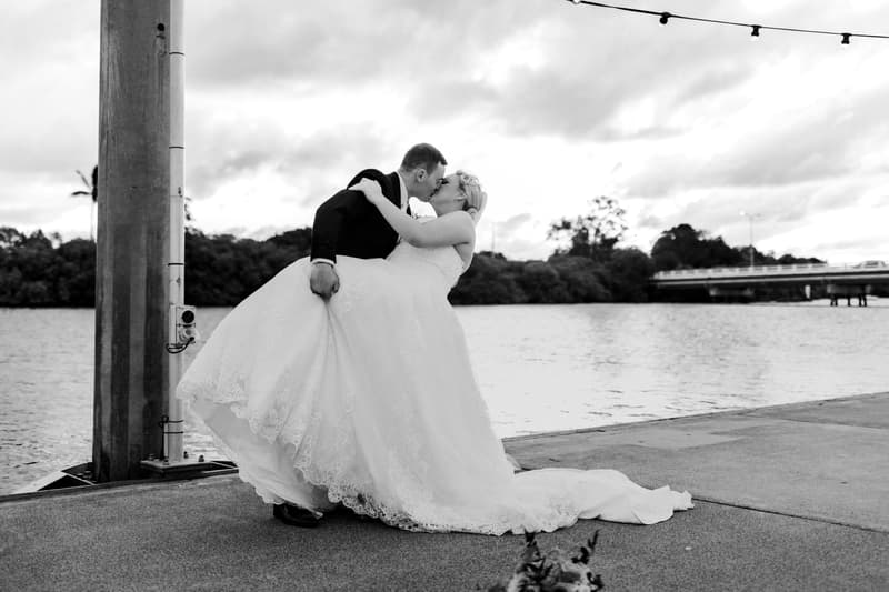 The groom stands at Sandstone Point Hotel waterfront with four groomsmen holding a veil above him.