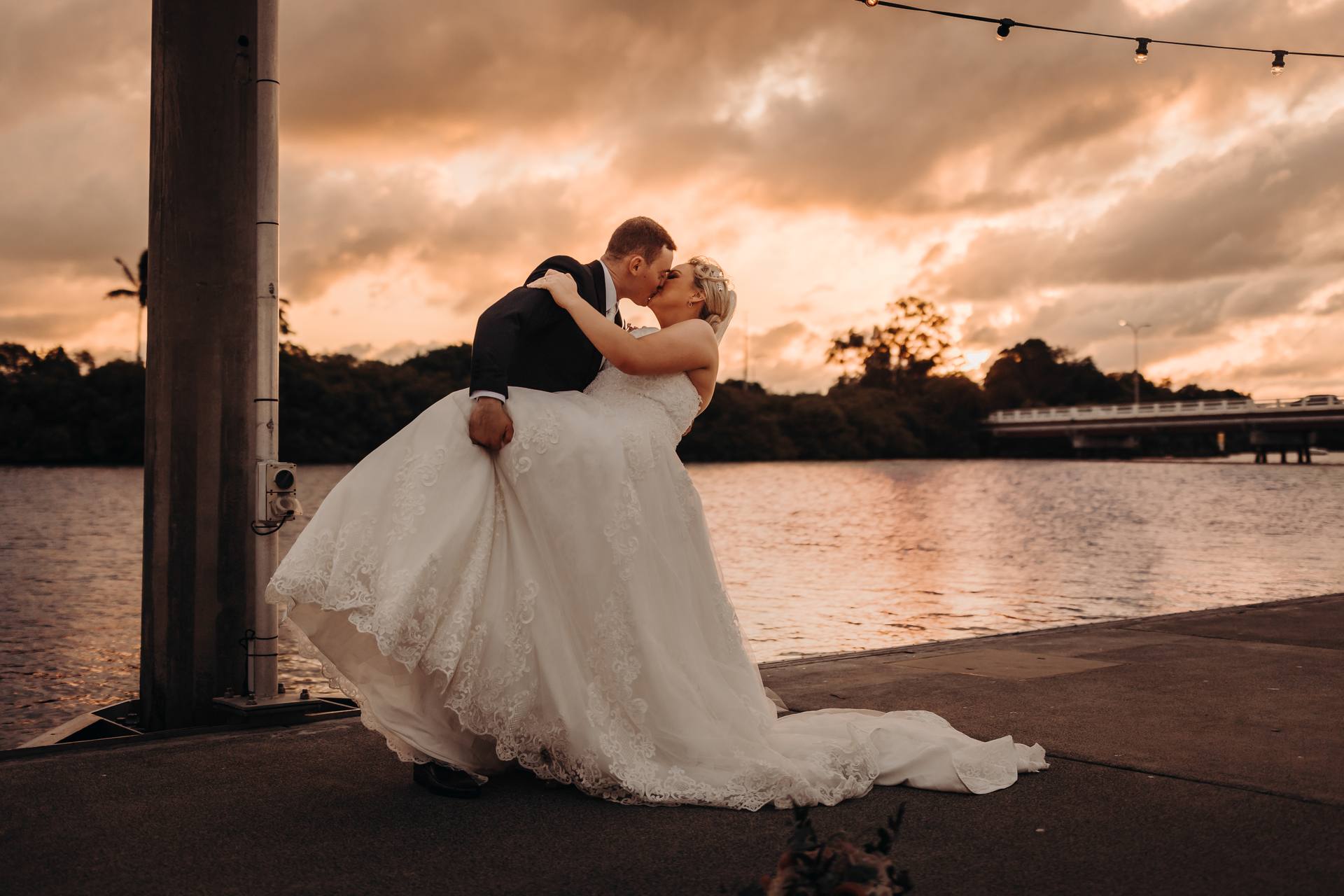 The groom dips the bride for a kiss beside the water at Sandstone Point Hotel during sunset.