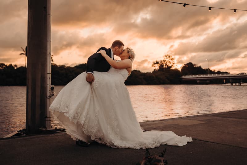 The groom dips the bride for a kiss beside the water at Sandstone Point Hotel during sunset.