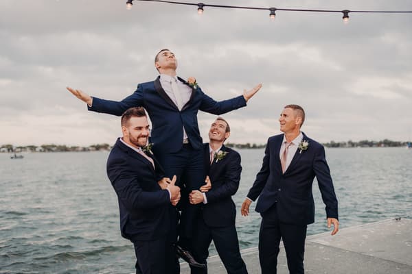 Dylan the groom is lifted by three groomsmen on a pier. Brisbane wedding videography by She Said Yes.