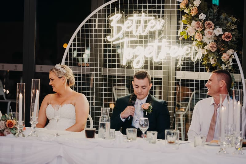 Emily and Dylan share a dance on the dance floor at the Sandstone Point Hotel — Pumicestone Room reception, with seated guests watching in the background.