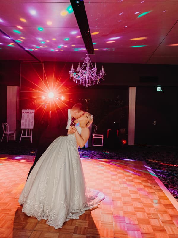The bride and groom share a kiss while dancing on the illuminated dance floor at the Sandstone Point Hotel — Pumicestone Room during their wedding reception.