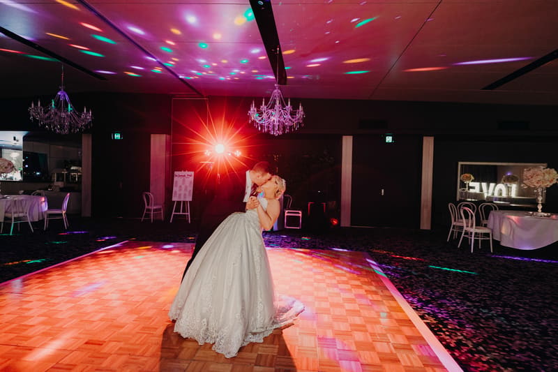 The bride and groom share a kiss while dancing on the illuminated dance floor at the. Photo and video packages by She Said Yes.
