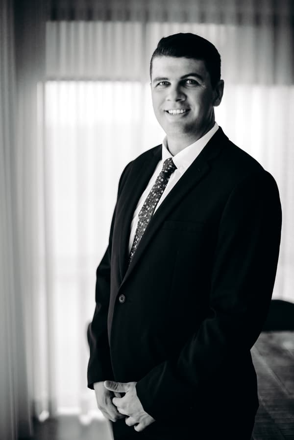 The groom Brent poses indoors at Preston Peak Winery Functions Centre wearing a dark suit and patterned tie, standing in front of sheer curtains.