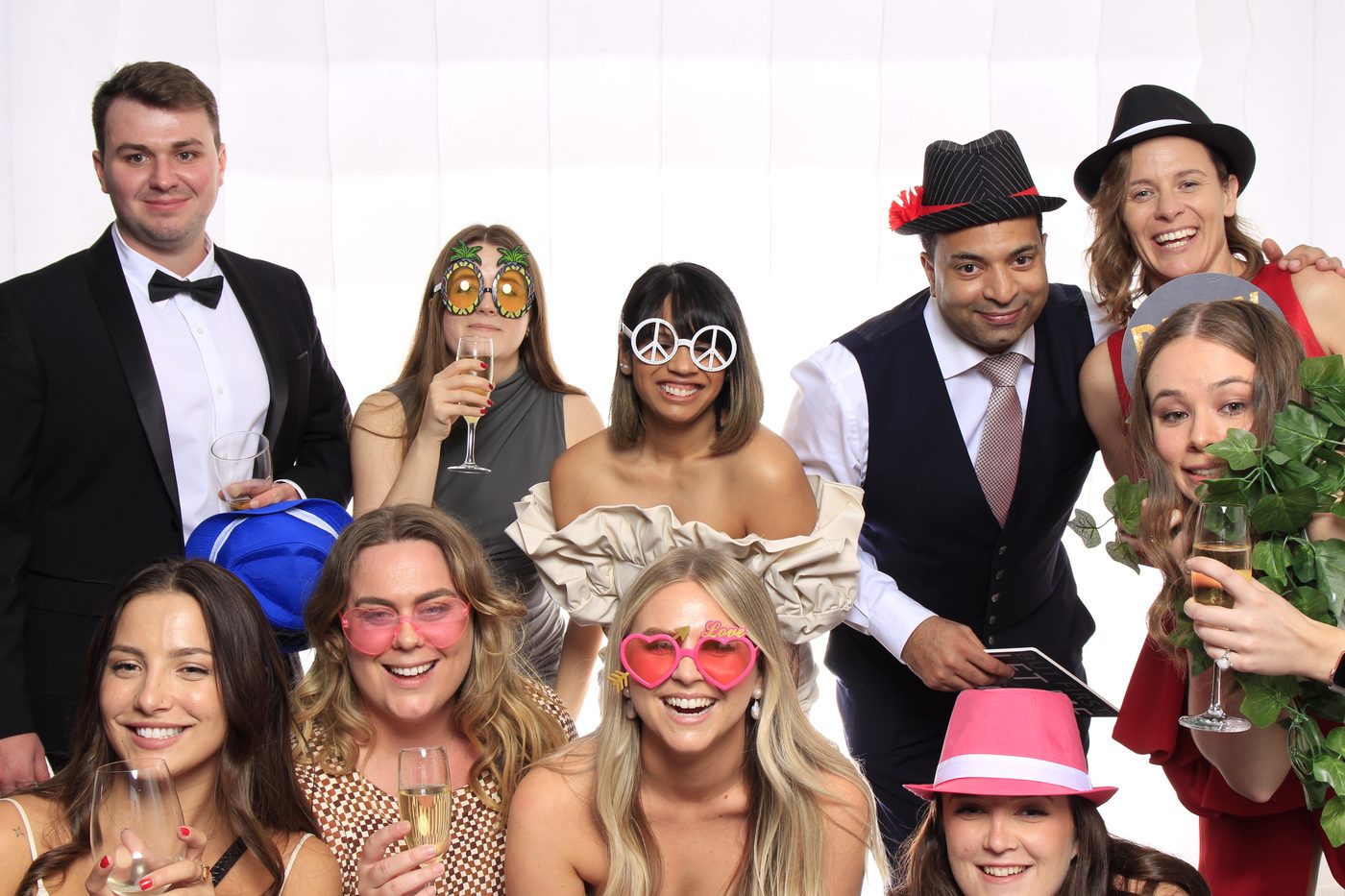Group of guests posing with playful props and drinks in a photo booth.