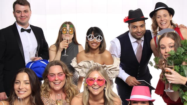 Group of guests posing with playful props and drinks in a photo booth.
