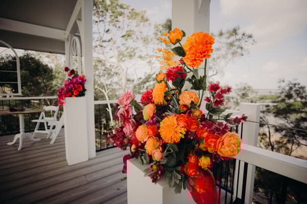 Floral arrangements with orange and pink flowers decorate the Pavilion at Sandstone Point Hotel during the wedding ceremony.