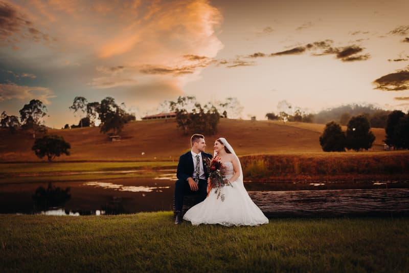 Bride Lilly and groom Connor sit on a log by a pond at Yabbaloumba Retreat during their couple portraits session at sunset.