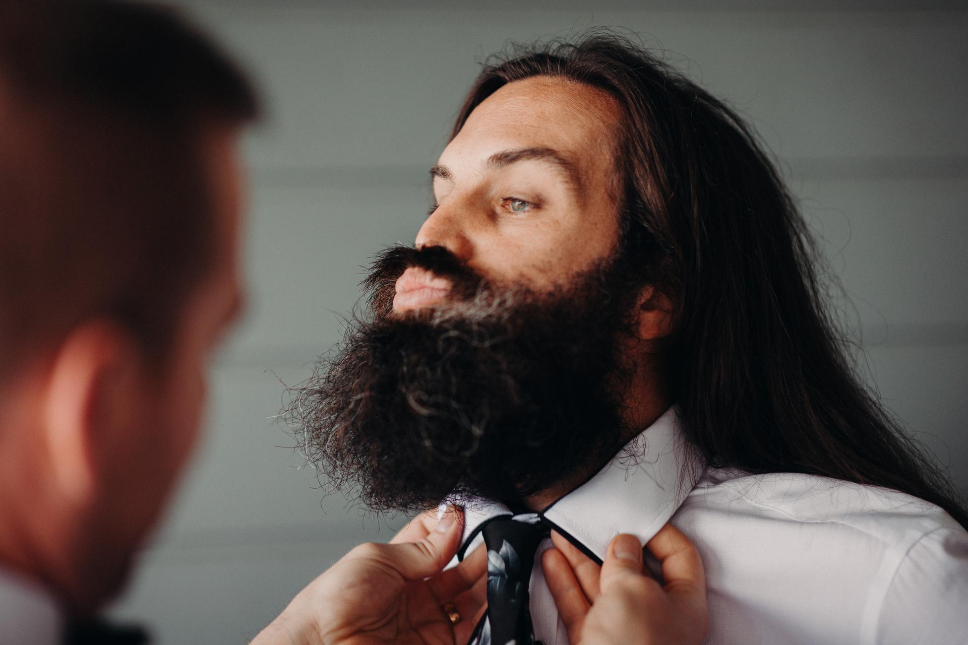 The groom is having his tie adjusted by another person during preparation.