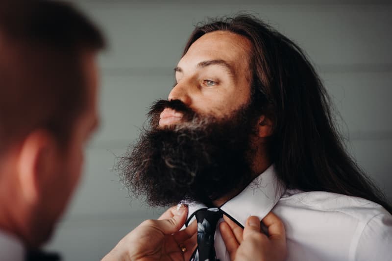 The groom is having his tie adjusted by another person during preparation.