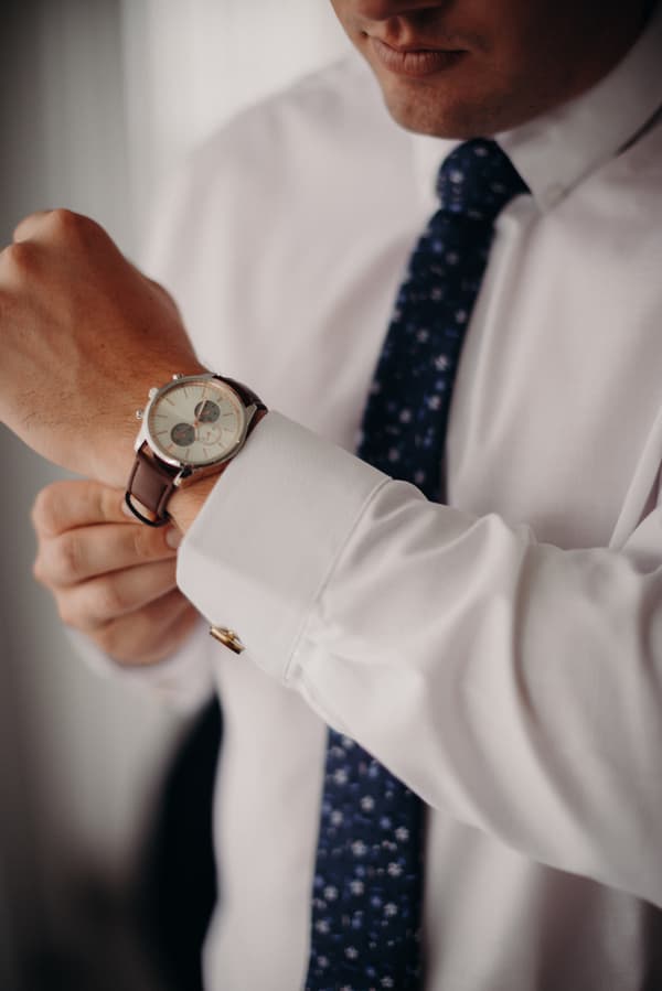 The groom at Preston Peak Winery Functions Centre adjusts his wristwatch while wearing a white dress shirt and a patterned blue tie.