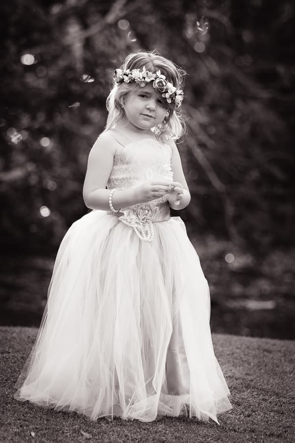 A young flower girl wearing a floral crown and a long tulle dress stands outdoors on grass at Novotel Sunshine Coast Resort.
