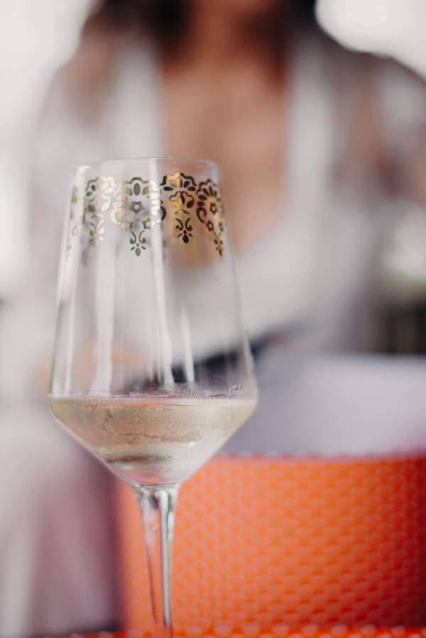 Close-up of a wine glass with white wine and gold decorative pattern at Preston Peak Winery Functions Centre, with a blurred figure in the background.