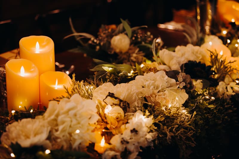 Close-up of floral centerpiece with white flowers, greenery, and lit candles at Ocean View Estates reception stage.