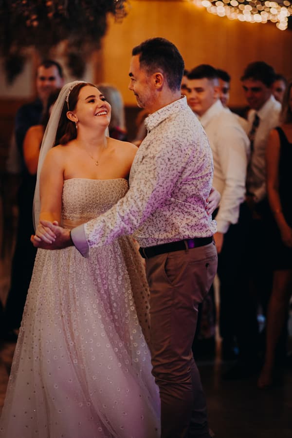 The bride Lilly dances with an older man at the reception stage of Yabbaloumba Retreat — The Shed, with guests watching in the background.