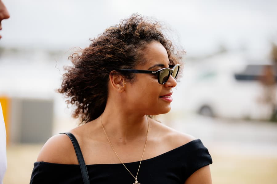 Person with curly hair and sunglasses smiling at Shorncliffe beachfront, Brisbane.