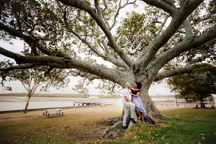 Couple sitting under a large tree, smiling at each other at Shorncliffe beachfront.
