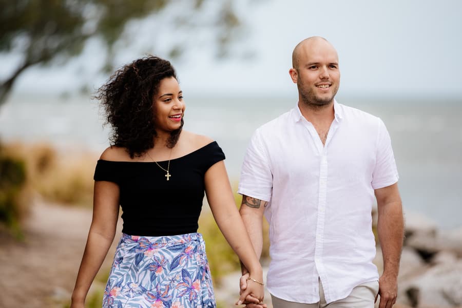 Couple walking hand in hand along the beach path with the sea in the background.