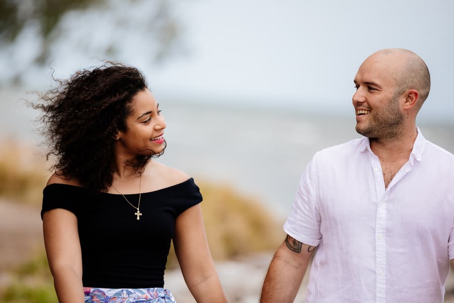 The couple smiling at each other while walking along the beach path.