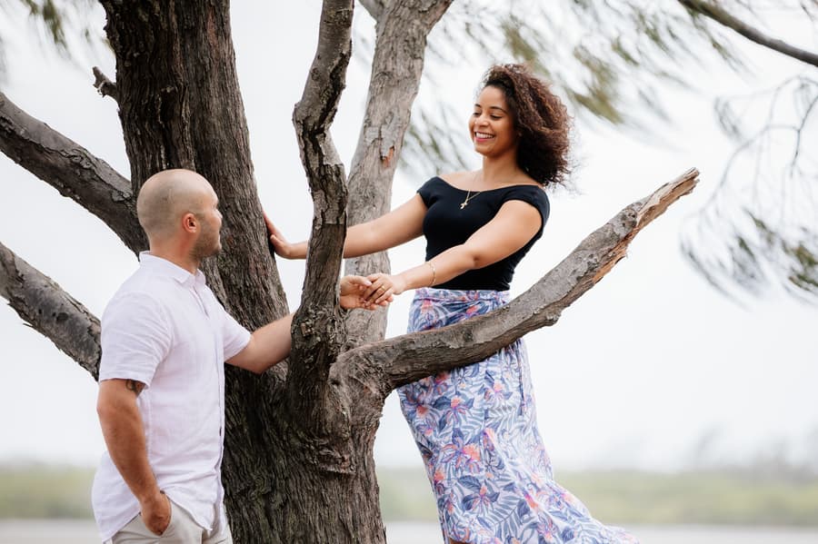 The couple holding hands, one standing on a tree branch, both smiling.