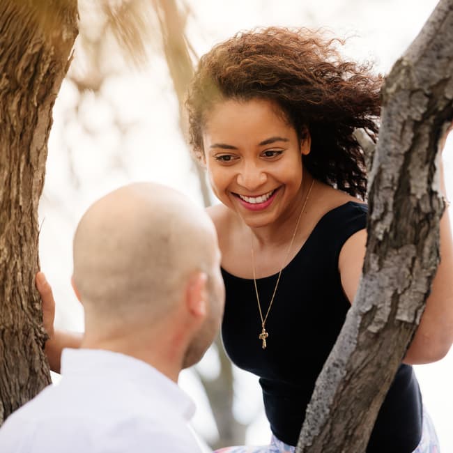 Person smiling at their partner while sitting on a tree branch.